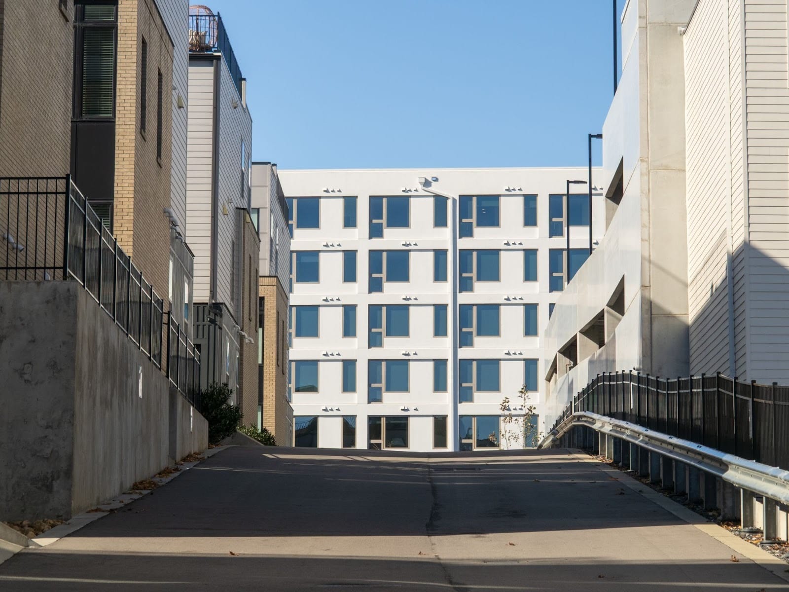 Uphill view along a driveway lined with townhomes, revealing the hilly terrain of Wedgewood-Houston, with a modern apartment building visible beyond.